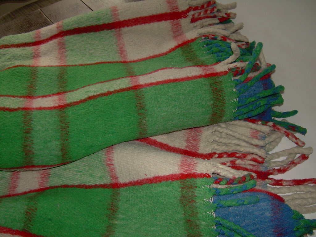 A thick cream wool blanket checked in green and red, with fringed ends