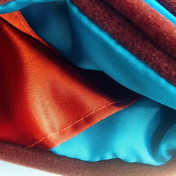 Close-up of polyester lining fabrics, an orange satin and a teal twill, beside a brushed pile fabric