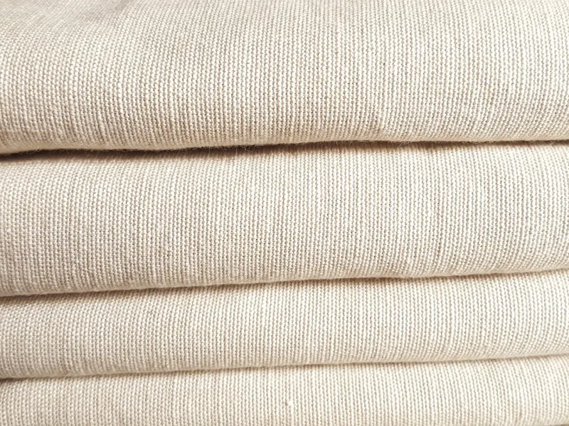 Folded layers of undyed, oatmeal-coloured plain-woven fabric in a stack
