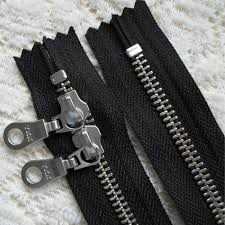 Two black zippers with silver metal teeth on lace, one of them carrying two sliders side by side