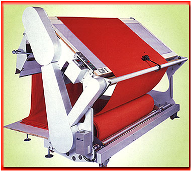 A fabric inspection machine: red fabric runs from a roll at the bottom up over an inclined viewing board and back down, with the machine's drive housing and controls on the left side